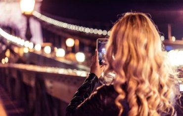 Blondes Mädchen fotografiert in der Nacht mit ihrem Smartphone eine erleuchtete Brücke